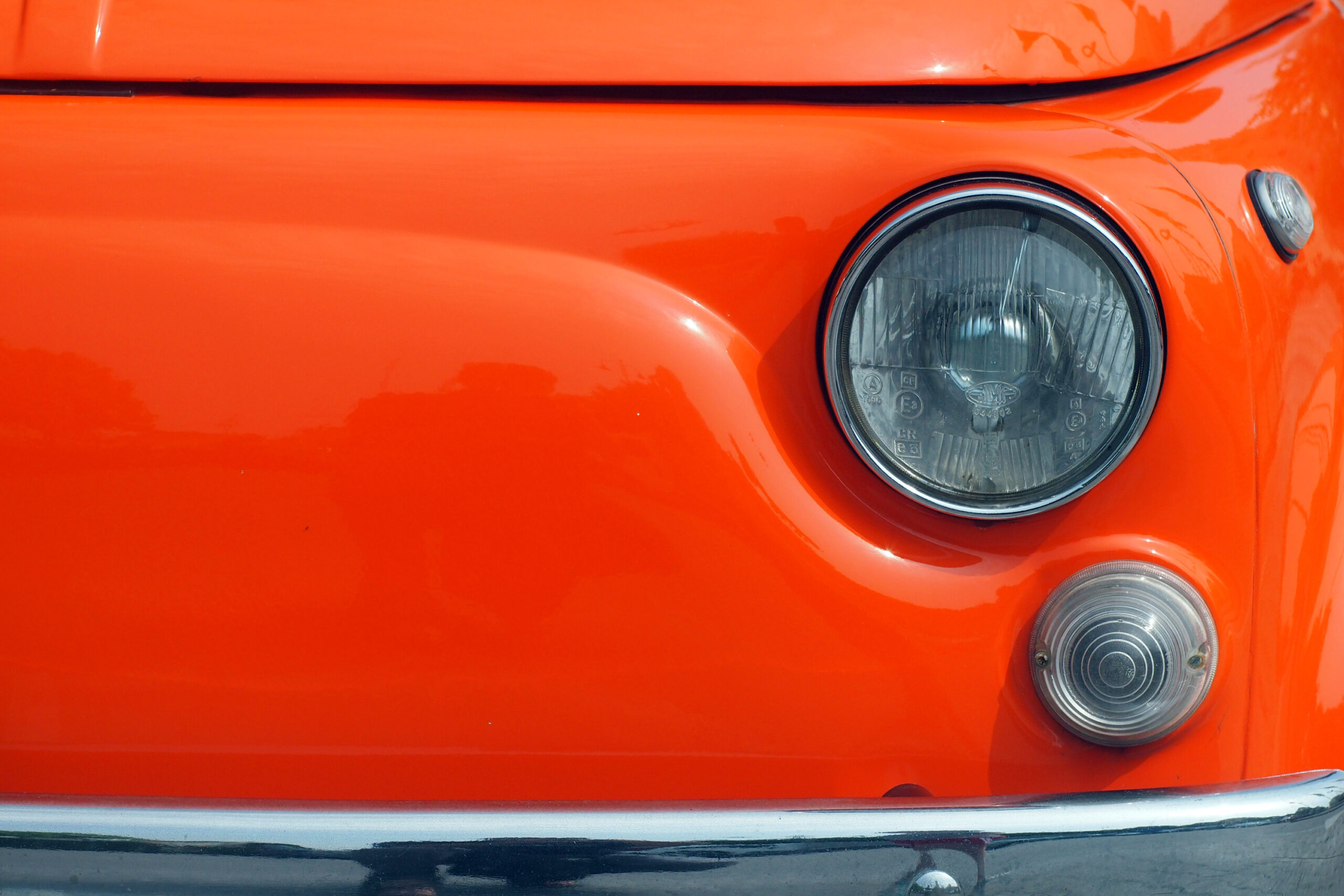Close-up of an orange Fiat car's front headlight and turn signal, highlighting the details necessary for Fiat mechanic and servicing.